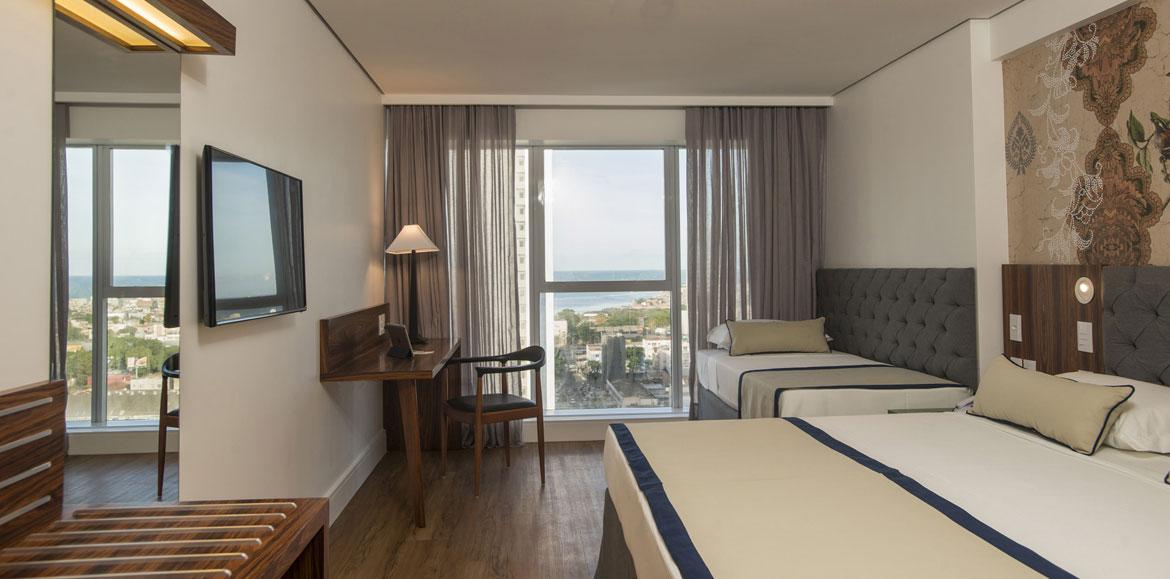 Hotel Luzeiros Recife Luaran gambar The photo shows a modern hotel room. It features two beds with a simple design, one larger and one smaller. There's a large window with sheer curtains, allowing natural light to fill the space and offering a view of the outside. A wooden desk and cha