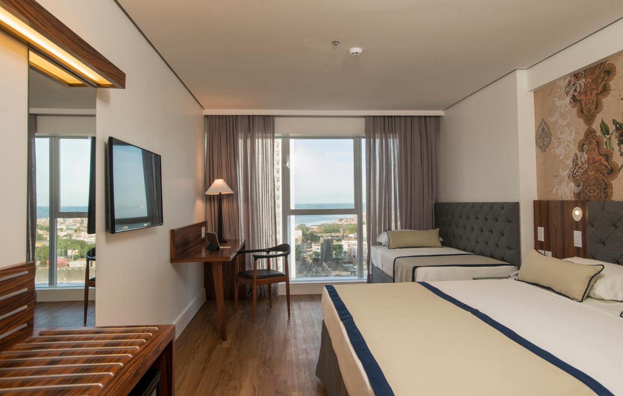 Hotel Luzeiros Recife Luaran gambar The photo shows a hotel room that features a modern and comfortable design. There are two beds: one larger bed and a smaller twin bed. The room has large windows with curtains that allow natural light to enter, offering a view of the outside, possibl